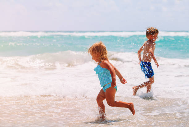 istock little girl and boy run play with waves on beach 653867610