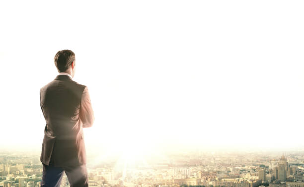 istock Businessman standing with back against morning city 653871174