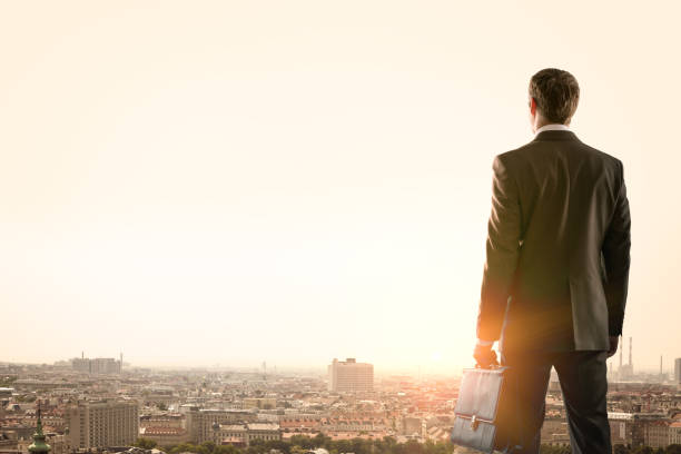 istock Businessman standing with back against morning city 653871188