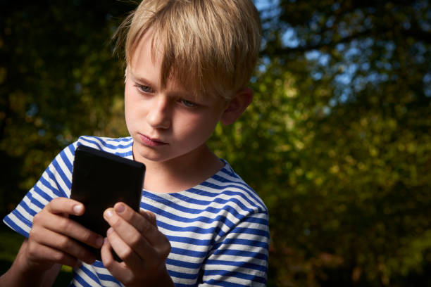 istock Child boy lying on grass in park and using smart phone 653873786