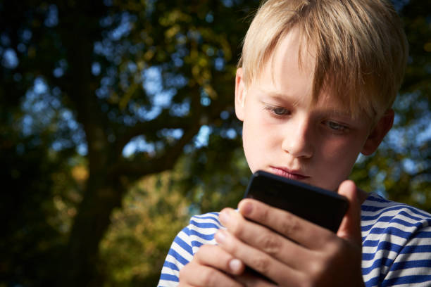 istock Child boy lying on grass in park and using smart phone 653873832