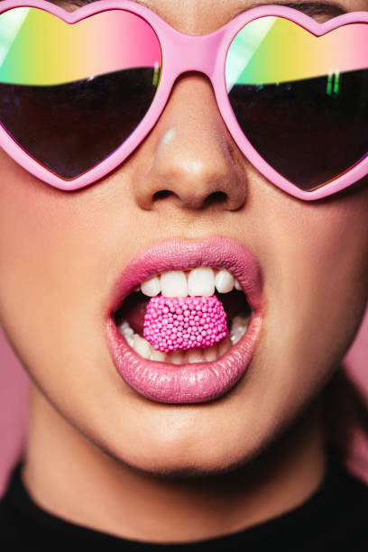 Beautiful woman holding candy in mouth Closeup portrait of young woman wearing heart shaped sunglasses holding candy in mouth. Beautiful pink lips with a piece of sweet candy. candy in mouth stock pictures, royalty-free photos & images