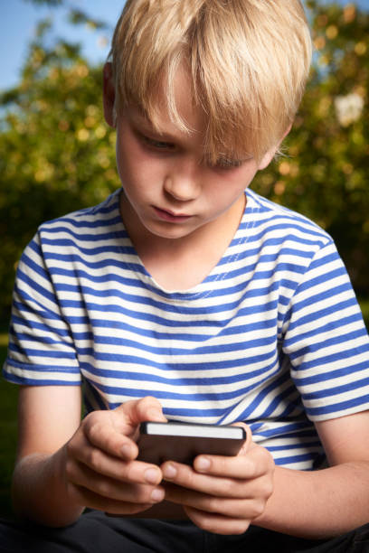 istock Child boy lying on grass in park and using smart phone 653873926