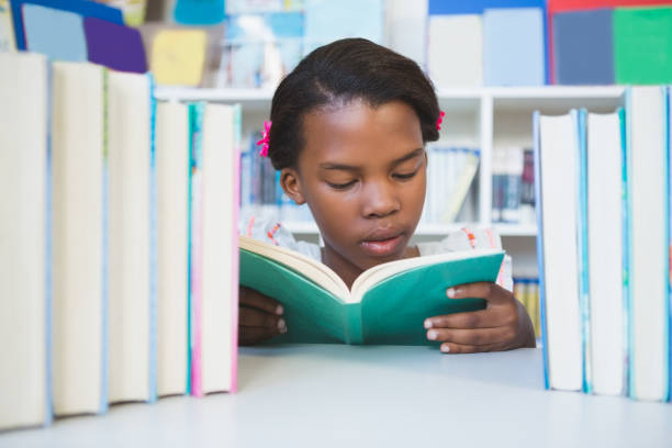 istock Schoolgirl sitting on table and reading book in library 653879872