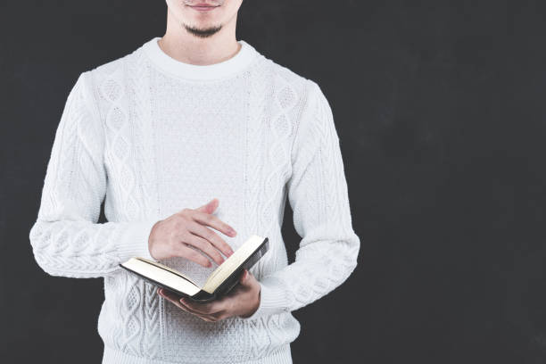 istock Young Japanese man wearing a white cable knit with a book 653882562