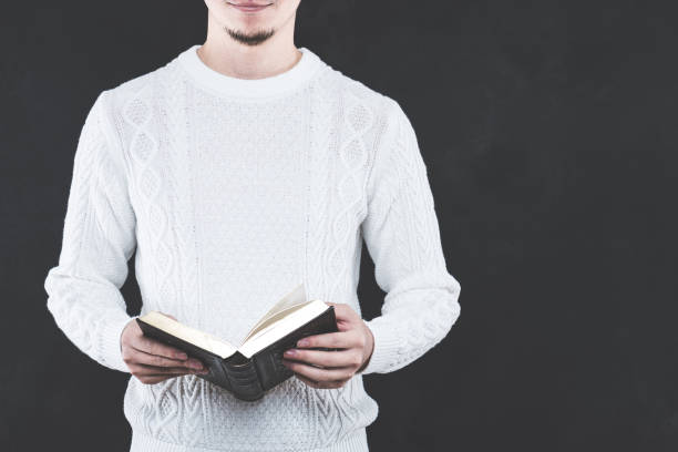 istock Young Japanese man wearing a white cable knit with a book 653882600