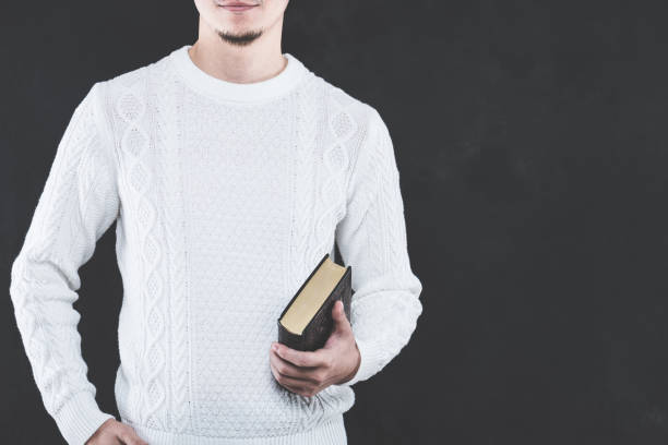 istock Young Japanese man wearing a white cable knit with a book 653882618