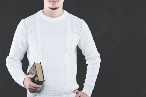 istock Young Japanese man wearing a white cable knit with a book 653882624