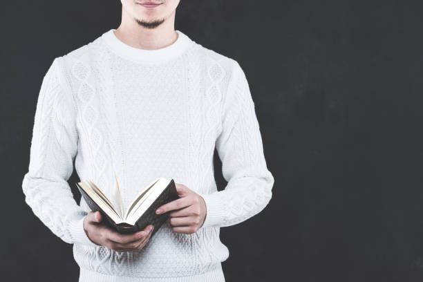 istock Young Japanese man wearing a white cable knit with a book 653882628