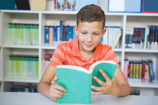 istock Schoolboy sitting on table and reading book in library 653892674