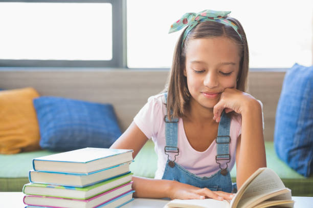 istock Schoolgirl sitting on table and reading book in library 653893414