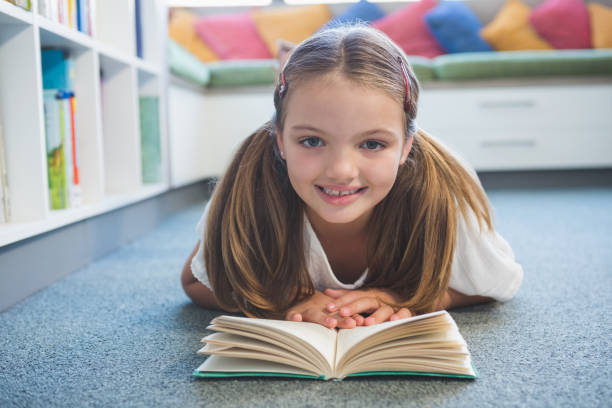 istock Schoolgirl lying on floor and reading a book in library 653894988