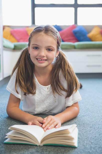 istock Schoolgirl lying on floor and reading a book in library 653895098