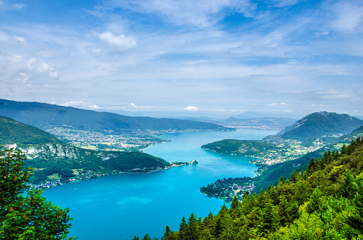 The photo shows a mountain panorama of Lake Annecy in France. The photo was taken outdoors on a sunny summer's day with blue sky and copy space.