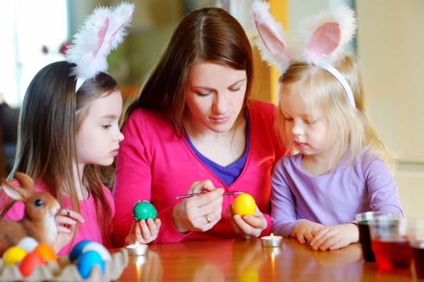 istock Young mother and her two daughters painting Easter eggs 653900892
