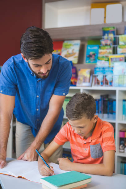 istock Teacher helping school kid with his homework in library 653908280