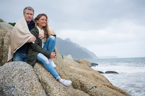 Couple wrapped in shawl sitting on rocks at the beach
