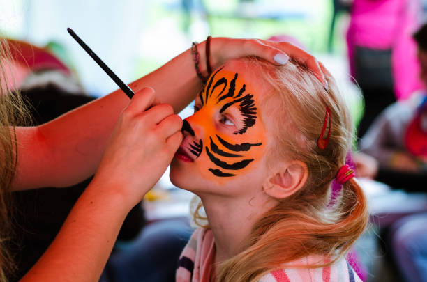 face painting little lovely blond girl beeing face painted to tiger cat face paint stock pictures, royalty-free photos & images