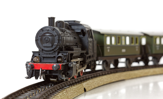 Vintage model electric train formed by a steam locomotive and green passenger cars on the rails