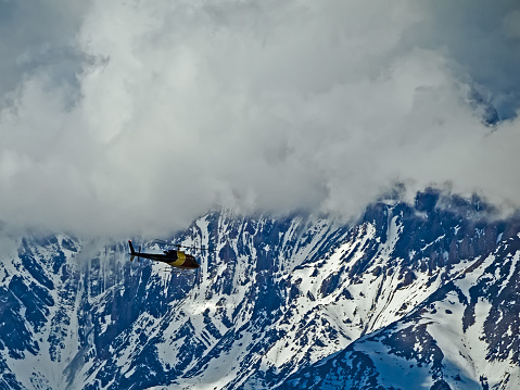 Rescue operation in  Annapurna conservation area аfter a snow storm. A multi-colored helicopter in flight, a background of snow-covered rocks. This photo was taken at an altitude of 4600m above sea level.