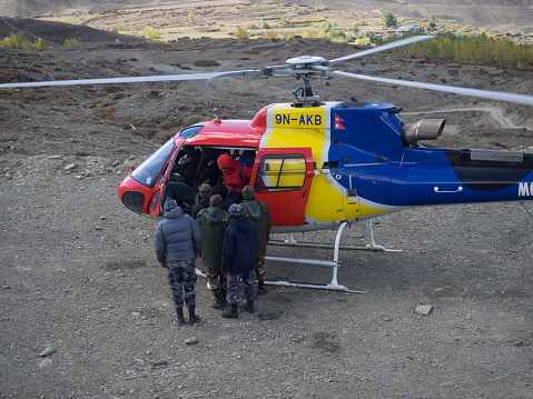 Rescue operation in  Annapurna conservation area аfter a snow storm. A multi-colored helicopter stands on the landing pad. From the helicopter comes the rescued tourist in a red jacket. Near the helicopter are soldiers of the army of Nepal, who take part in the operation for the rescue