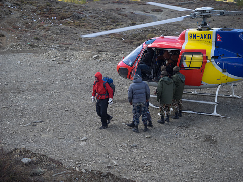 Rescue operation in  Annapurna conservation area аfter a snow storm. A multi-colored helicopter stands on the landing pad. A man in a red jacket is a rescued tourist. Near the helicopter are soldiers of the army of Nepal, who take part in the operation for the rescue.