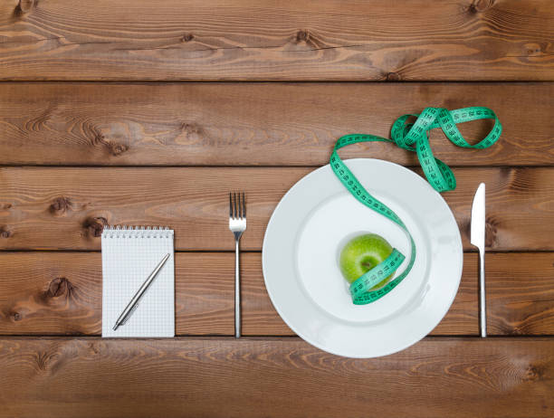 istock Green apple on plate with knife fork and measure tape 653963976