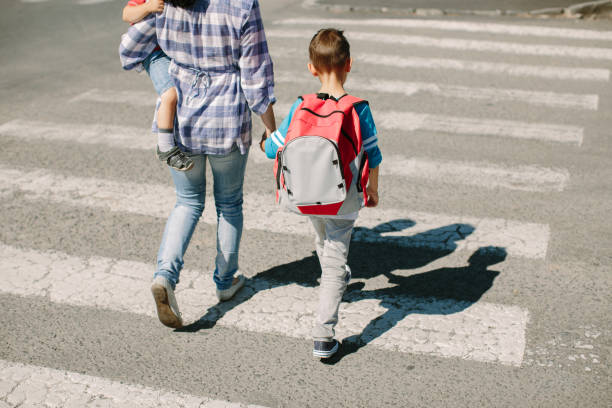 mutter und ihre kinder überqueren einer straße auf dem weg zur schule am morgen - rules of the road stock-fotos und bilder