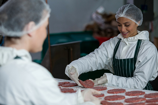 Female butchers processing hamburger patty at meat factory