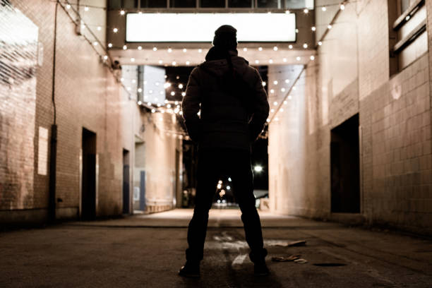 silhouette of a man standing in the dirt and dark alley at night.