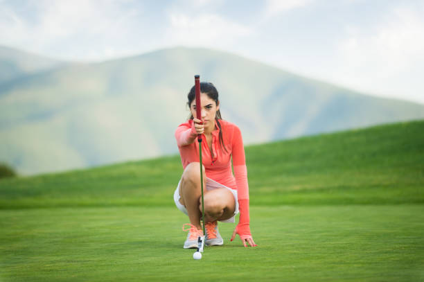 A young Hispanic women playing golf, on the putting green ready to sink it.