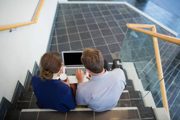 istock Businessman and woman sitting on steps using laptop 653978996