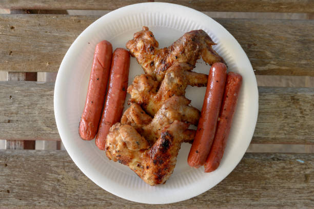 Grilled marinated chicken sausages and wings on white polystyrene plate. top view