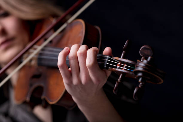 closeup of a violinist's hand playing Young beautiful woman violinist player playing her instrument on her shoulder holding bow. portrait in a blurred dark room in background. Concept of classical music folk stock pictures, royalty-free photos & images