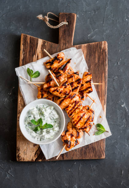 상위 뷰 어두운 배경에 나무 절단 보드에 tzatziki 소스와 구운된 닭 꼬치 - grilled barbecue chicken meat 뉴스 사진 이미지