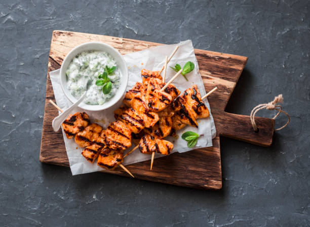 a la parrilla brochetas de pollo teriyaki y salsa tzatziki sobre una plancha de madera sobre un fondo oscuro, la vista superior. deliciosos aperitivos - roasted mint dinner vegetable fotografías e imágenes de stock