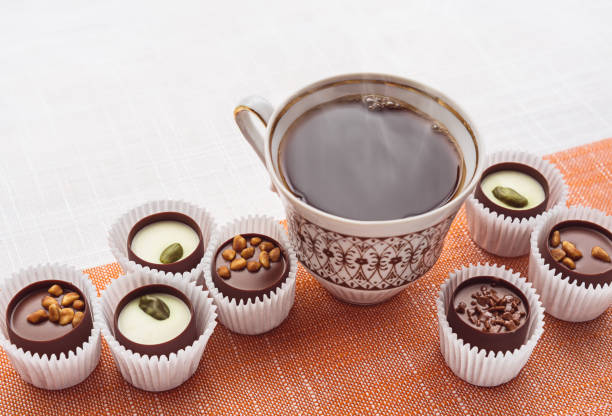 A cup of hot coffee and chocolate sweets on the tablecloth.
