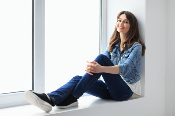 istock Smiling beautiful woman relaxing on window sill 654068044