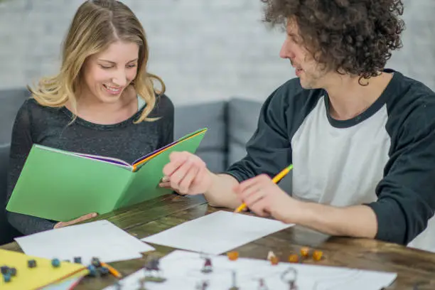 Two friends are playing a role-playing fantasy adventure game together in their living room indoors. They tell a story while playing the game and roll dice to make decisions and move figurines on a game board.