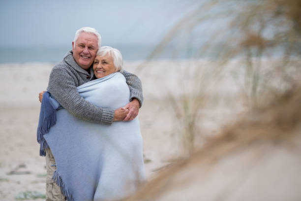 istock Senior couple wrapped in shawl on the beach 654079898
