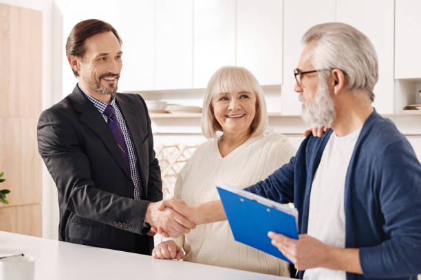 istock Cheerful real estate agent presenting contract to elderly couple 654083952