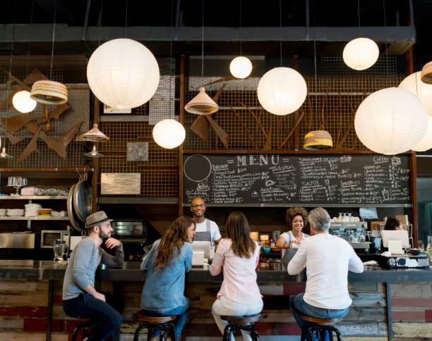 People at a cafe People at a cafe sitting at the bar counter and staff serving coffees - food service concepts people bar bar counter restaurant stock pictures, royalty-free photos & images