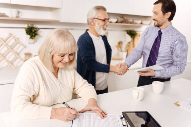 istock Retired woman signing contract while her husband greeting the notary 654091256