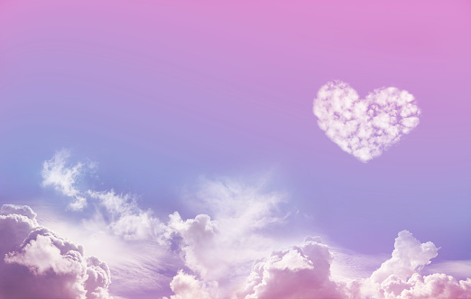 Wide Blue and Pink Sky Background with fluffy clouds along the bottom and one large isolated Love Heart Shaped cloud formation above on right hand side with plenty of copy space