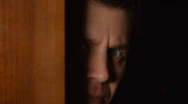 cara hombre mira desde una puerta de la oscuridad - hiding fear men peeking fotografías e imágenes de stock