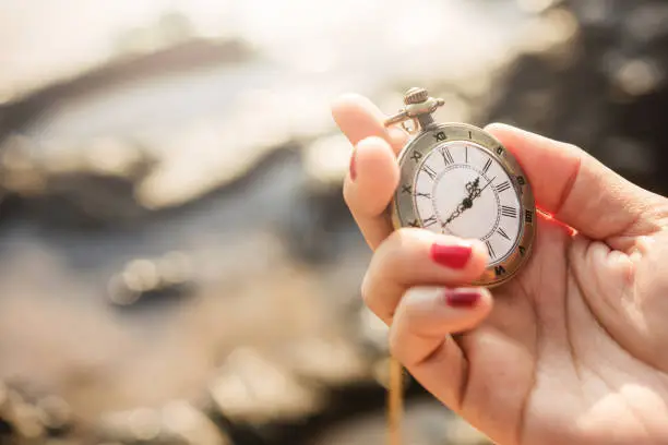 Vintage pocket watch in woman hand in sunrise or sunset, sea as background, Time and Aging concept