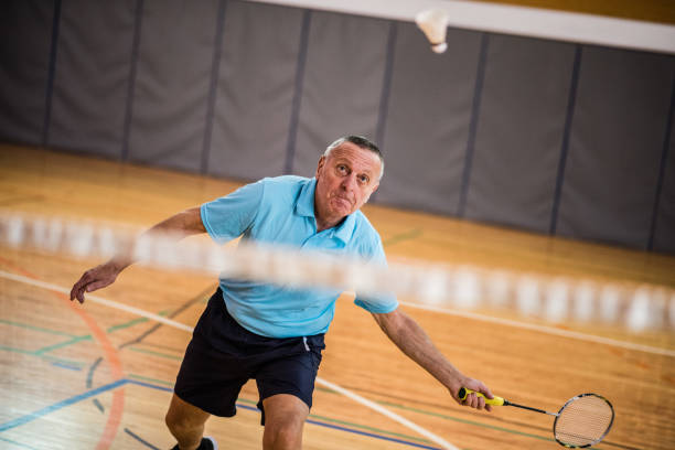 Man playing badminton Senior man hitting shuttlecock with badminton racquet in court. badminton racket stock pictures, royalty-free photos & images