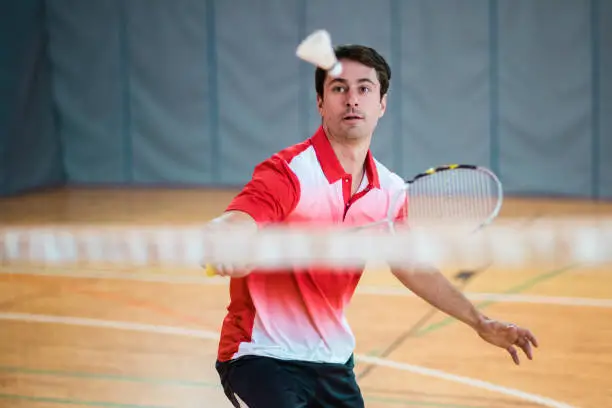 Mid adult man hitting shuttlecock with badminton racquet in court.