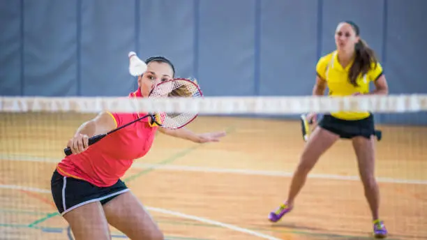 Woman hitting shuttlecock with badminton racquet, partner looking at her.