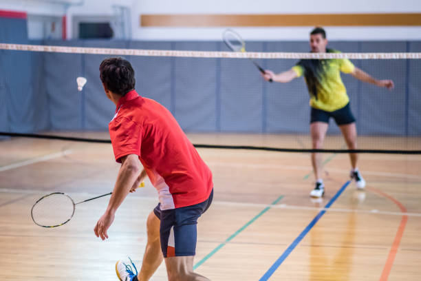 Man playing badminton Mid adult man hitting shuttlecock with badminton racquet in court. badminton stock pictures, royalty-free photos & images